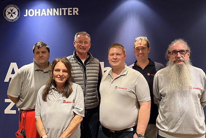 Eine Gruppe von Menschen schaut in die Kamera, darunter fünf Johanniter und ein Herr im Anzug.